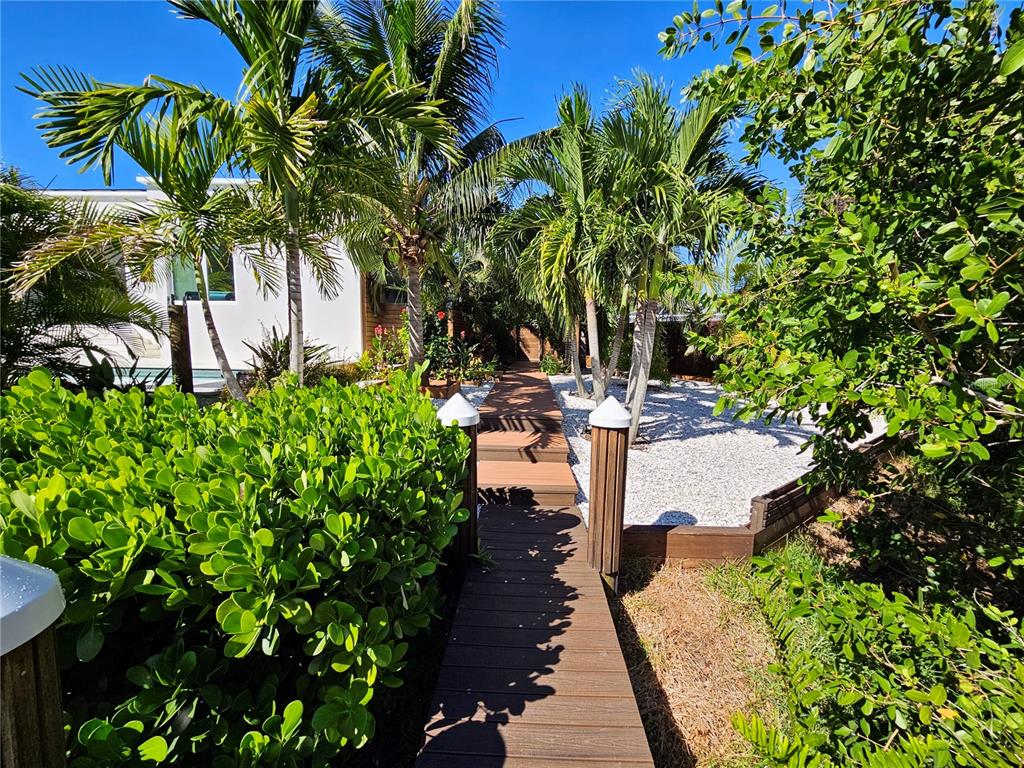 A wooden walkway leads through a landscaped yard with palm trees and white gravel — 2408 NASSAU STREET, SARASOTA, FL