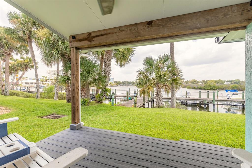 A covered deck overlooks a grassy lawn, palm trees, and a wooden dock on the water — 76 HEATHER POINT COURT, NEW SMYRNA BEACH, FL
