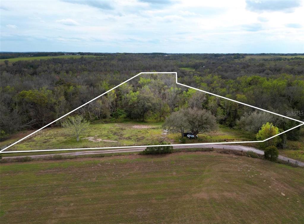 An aerial view shows a fenced, wooded lot with a dirt road in the foreground — 33234 CHIPCO RANCH ROAD, DADE CITY, FL
