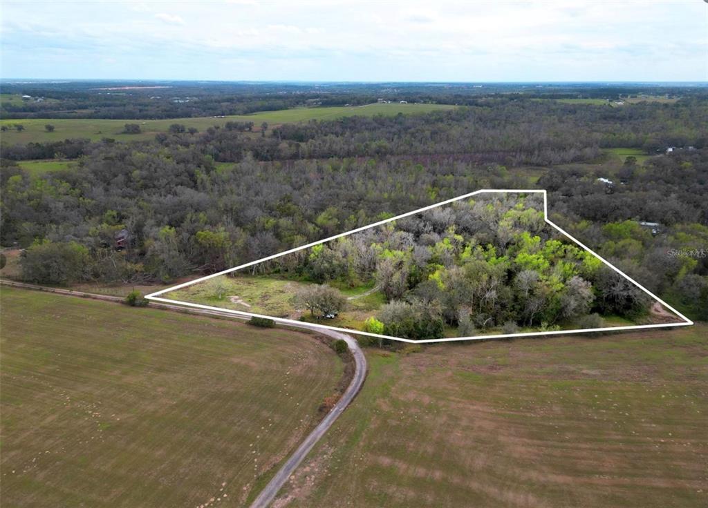 An aerial view shows a triangular plot of wooded land surrounded by open fields — 33234 CHIPCO RANCH ROAD, DADE CITY, FL