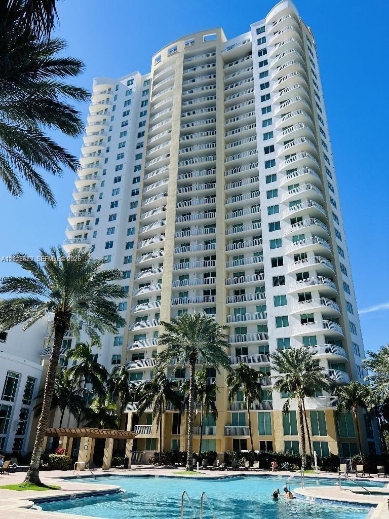 A tall residential high-rise building stands behind a swimming pool with palm trees — 1745 E Hallandale Beach Blvd # 2104W, Hallandale Beach FL 33009, HALLANDALE BEACH, FL