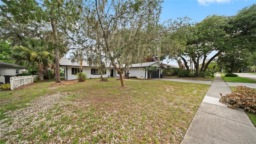 A white single-story house with a dark roof and garage sits behind a large tree — 2662 DERBYSHIRE ROAD, MAITLAND, FL