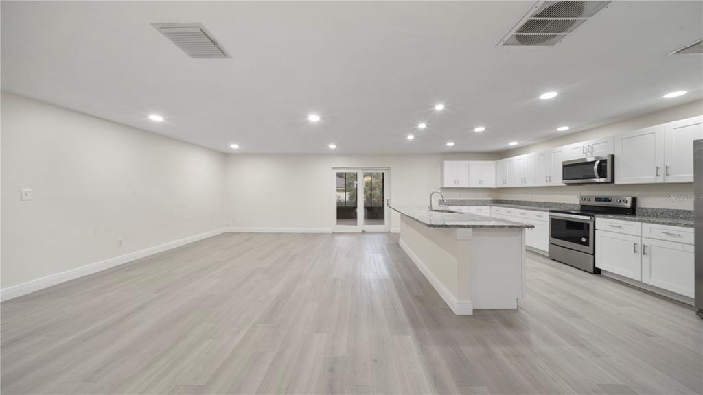 An open-concept kitchen and living area featuring white cabinets, granite countertops, and light wood flooring — 2662 DERBYSHIRE ROAD, MAITLAND, FL