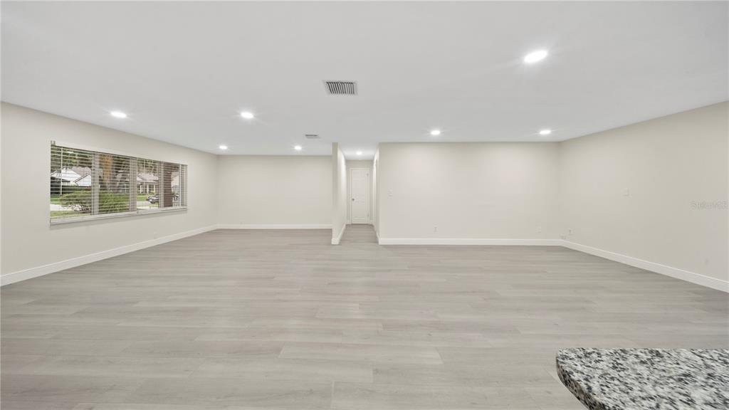 A spacious, empty room with light-colored wood-look flooring, recessed lighting, and a large window — 2662 DERBYSHIRE ROAD, MAITLAND, FL