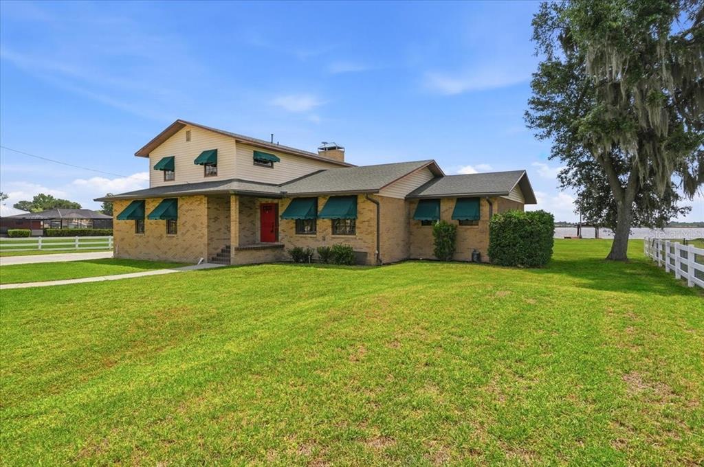A two-story brick and siding house with green awnings sits on a large grassy lawn — 2731 STATE ROAD 557, LAKE ALFRED, FL