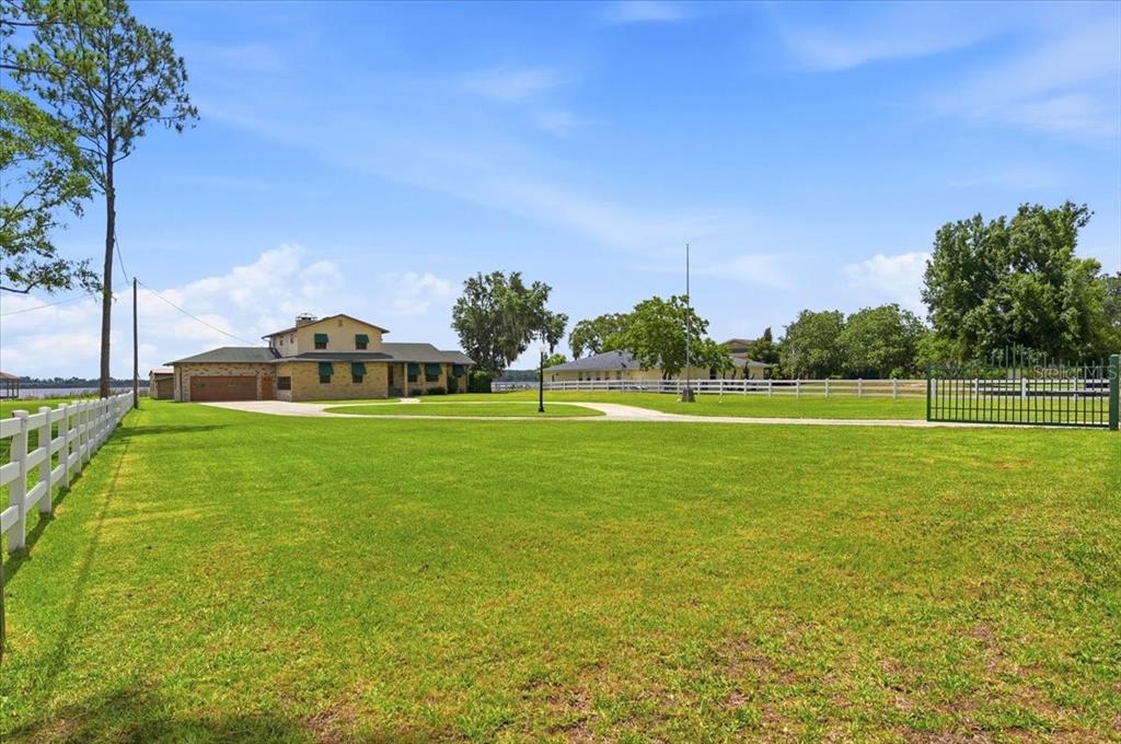 A large house with a brick garage sits on a grassy lot behind a fence — 2731 STATE ROAD 557, LAKE ALFRED, FL