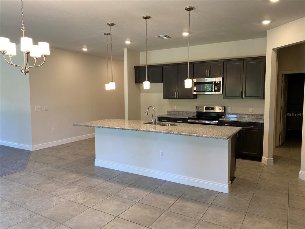 A kitchen features dark cabinets, granite countertops, a central island, and tile flooring — 2789 WENONA DRIVE, NORTH PORT, FL