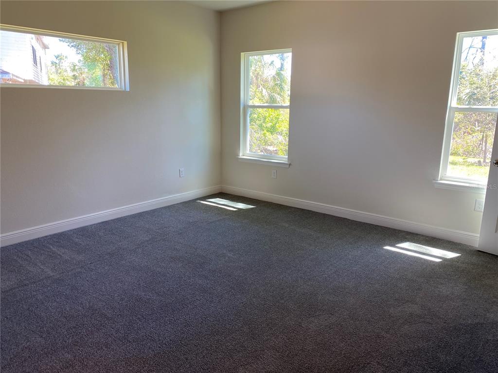 An empty bedroom with gray carpet, white walls, and three windows — 2789 WENONA DRIVE, NORTH PORT, FL
