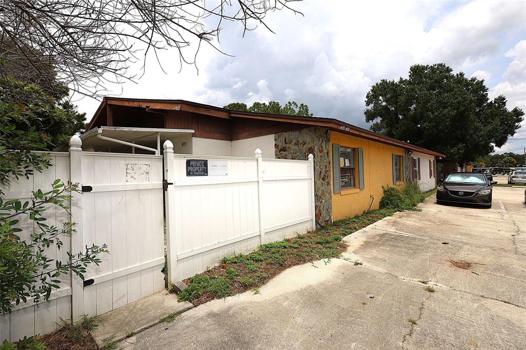 A single-story building with a yellow stucco facade, stone accents, and a white privacy fence — 4179 SPITFIRE AVENUE, KISSIMMEE, FL