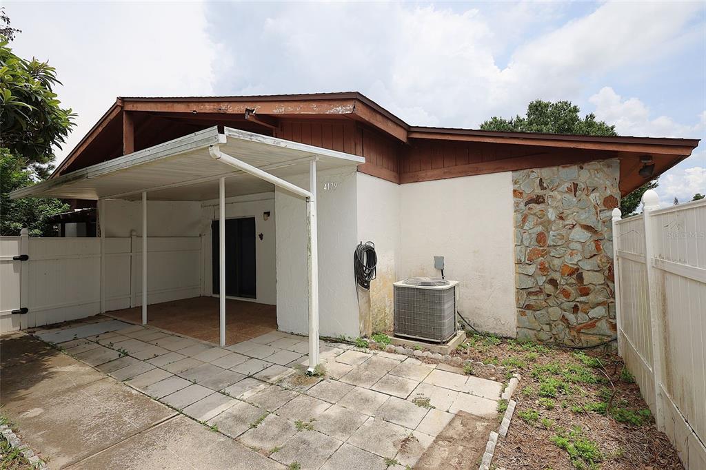 A backyard patio features a covered area, a stone accent wall, and an air conditioning unit — 4179 SPITFIRE AVENUE, KISSIMMEE, FL