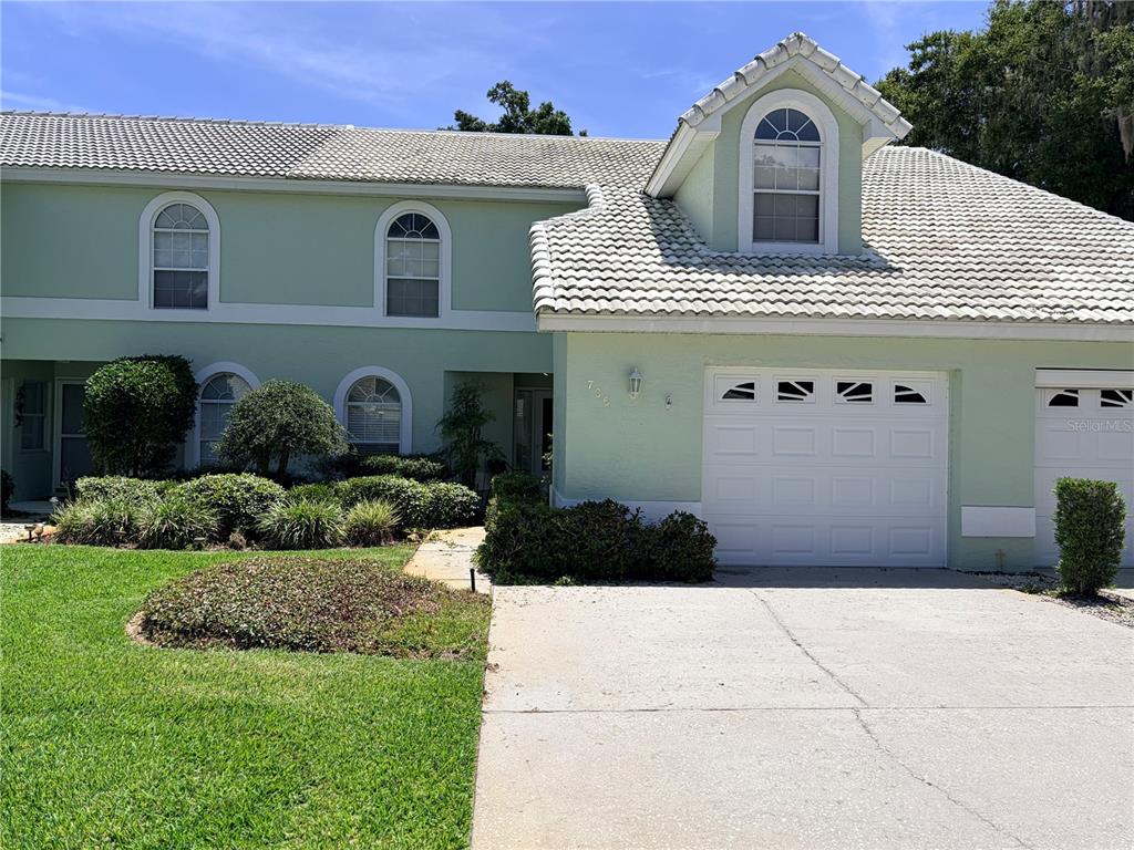 A two-story light green townhouse features a white garage door and a tiled roof — 706 MORAY DRIVE, INVERNESS, FL