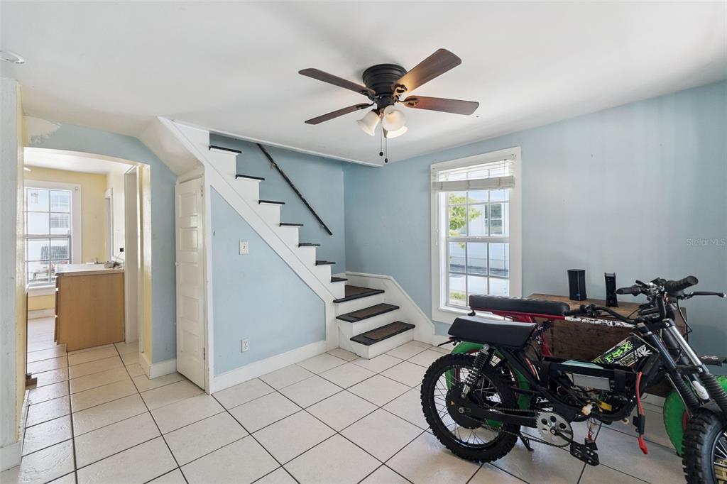 A room with light blue walls, white tile flooring, a staircase, and a motorized bicycle — 207 MARY AVENUE, NEW SMYRNA BEACH, FL