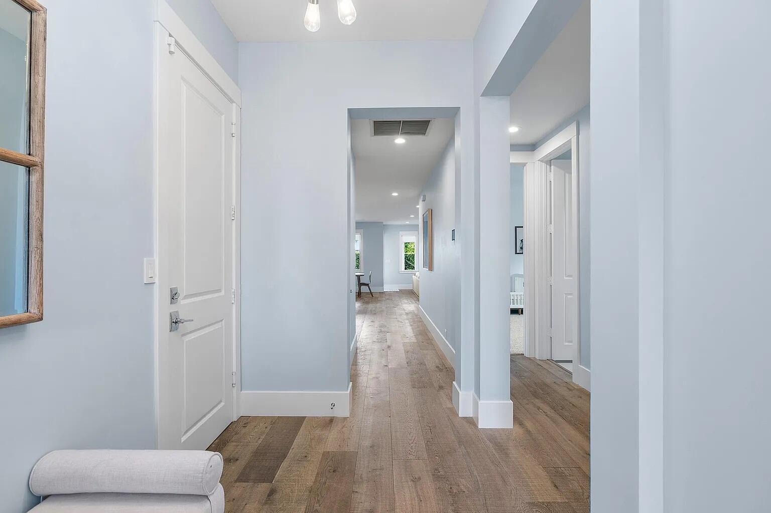 A hallway with light blue walls, white trim, and wood-look flooring leads to a living area — 1420 High Ridge Road, FL 33461, FL
