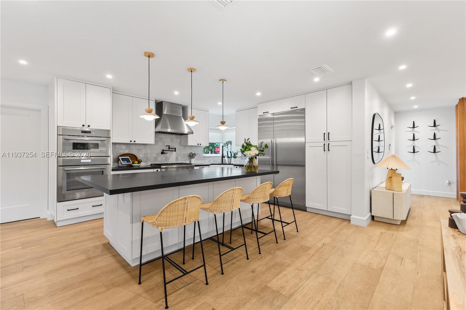 A modern kitchen features white cabinetry, a large black island, and four woven bar stools — 800 NE 72nd St, Miami FL 33138, MIAMI, FL