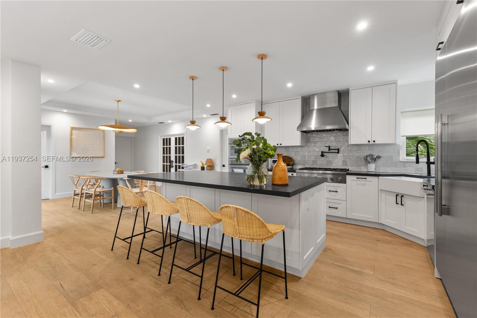A modern kitchen features a large island with wicker stools and white cabinetry — 800 NE 72nd St, Miami FL 33138, MIAMI, FL
