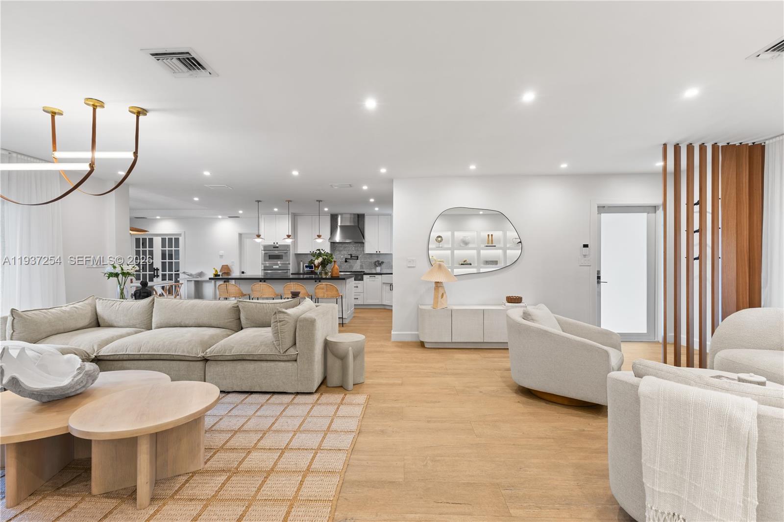 An open-concept living room features a large sectional sofa, light wood flooring, and a kitchen — 800 NE 72nd St, Miami FL 33138, MIAMI, FL