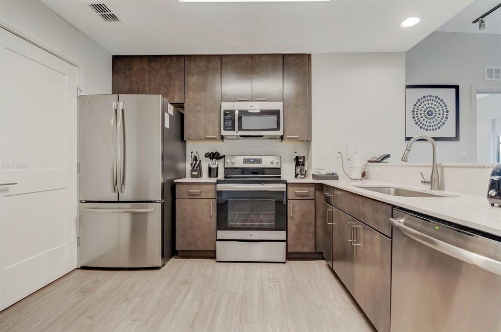 A kitchen features stainless steel appliances, dark wood cabinets, and light-colored wood-look flooring — 14501 GROVE RESORT AVENUE UNIT 3706, WINTER GARDEN, FL