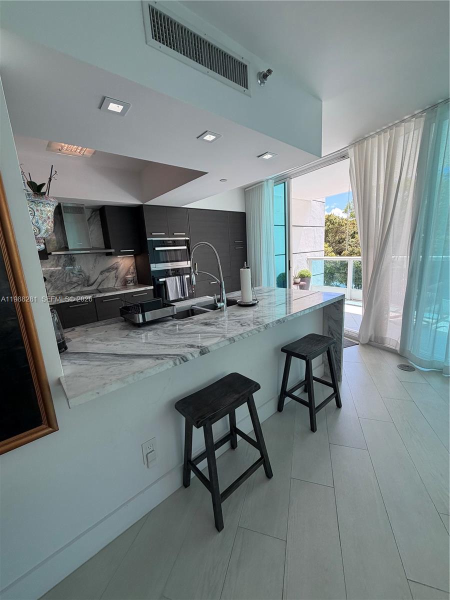 A modern kitchen features marble countertops, dark cabinetry, and a breakfast bar with two stools — 2127 Brickell Ave # 502, Miami FL 33129, MIAMI, FL