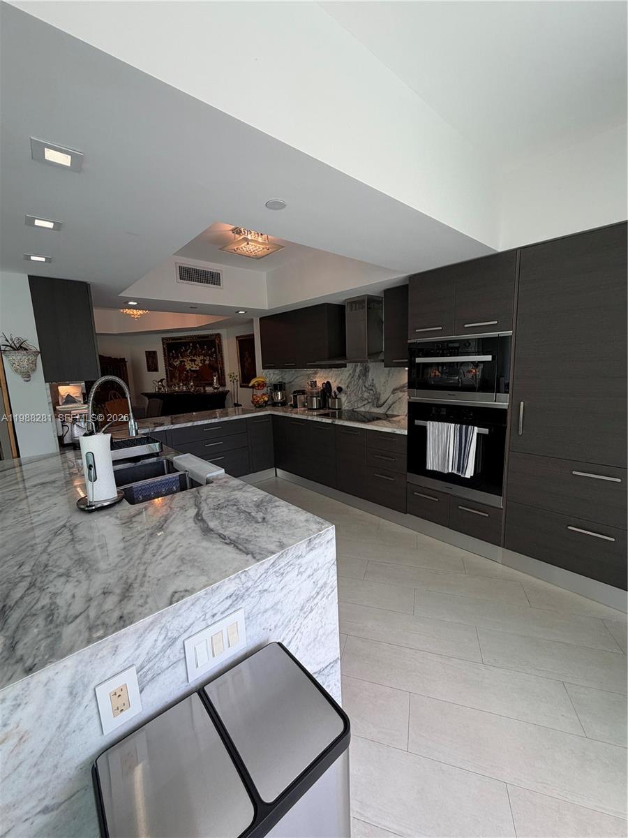 A modern kitchen features dark cabinetry, marble countertops, and a large central island — 2127 Brickell Ave # 502, Miami FL 33129, MIAMI, FL