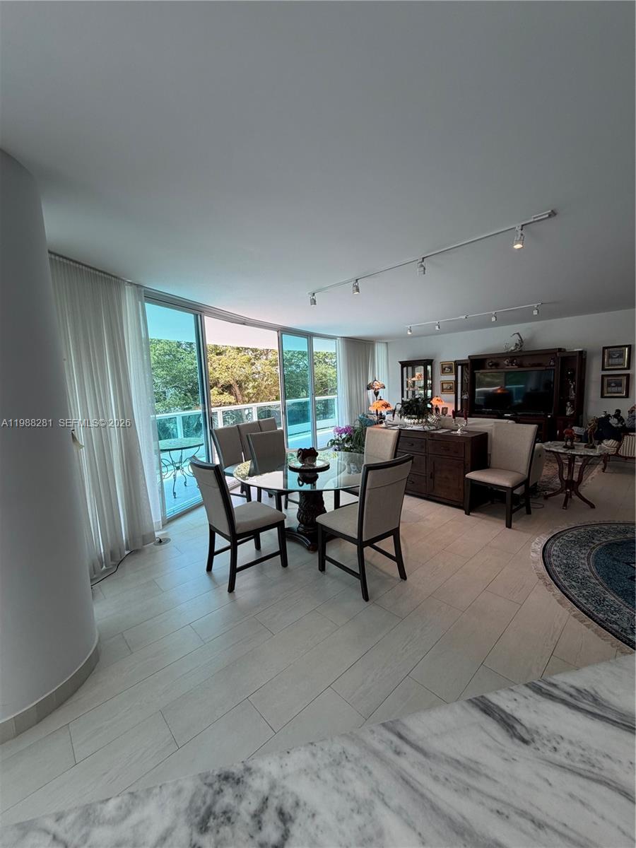 A dining area features a glass-topped table, upholstered chairs, and floor-to-ceiling windows overlooking trees — 2127 Brickell Ave # 502, Miami FL 33129, MIAMI, FL