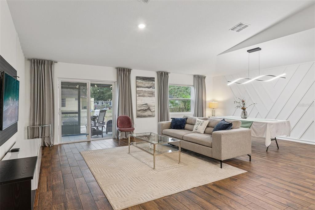 A living and dining area features wood-look tile floors, a glass coffee table, and wall paneling — 1830 RADCLIFF AVENUE SE, PALM BAY, FL