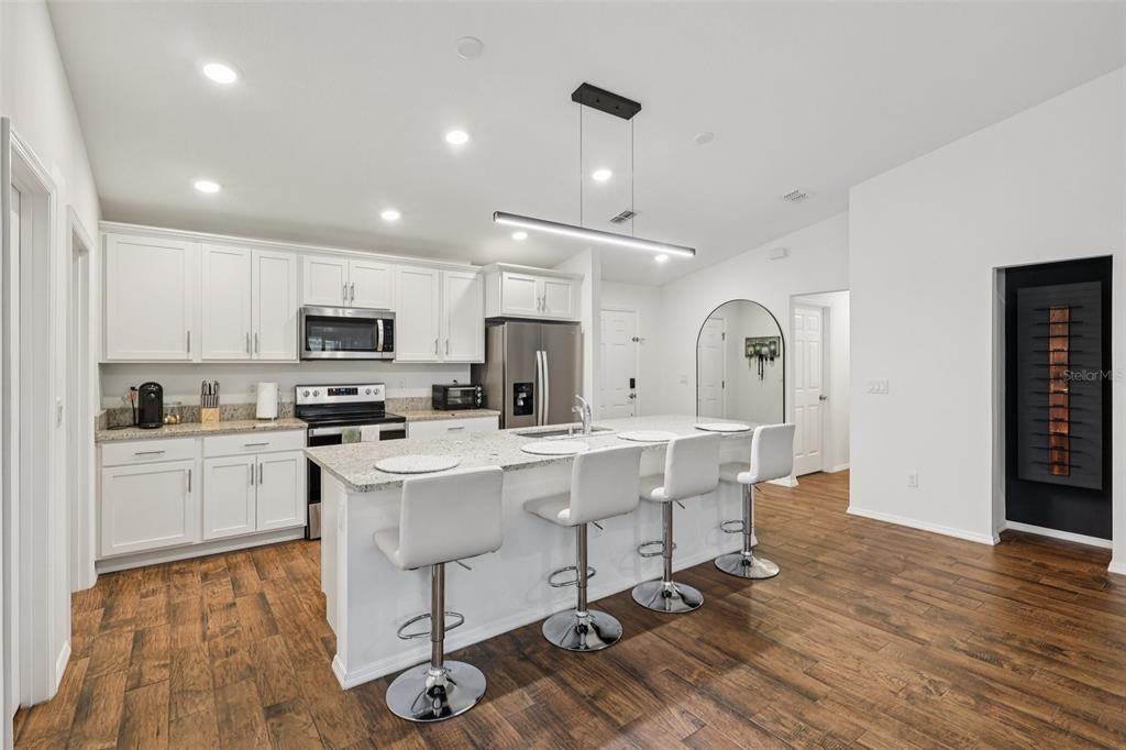 A modern kitchen features white cabinets, granite countertops, a central island with stools, and wood flooring — 1830 RADCLIFF AVENUE SE, PALM BAY, FL