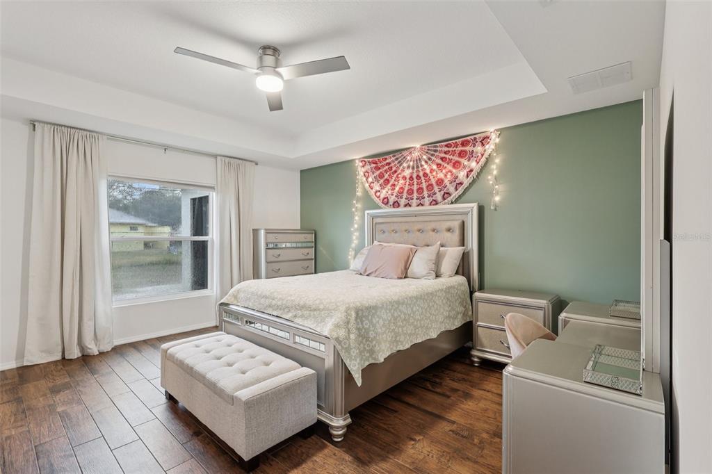 A bedroom features a bed with a green accent wall, wood flooring, and a ceiling fan — 1830 RADCLIFF AVENUE SE, PALM BAY, FL