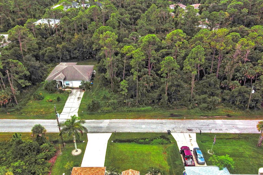 An aerial view shows a single-story house surrounded by dense woods next to a road — SHAFFER AVENUE, NORTH PORT, FL