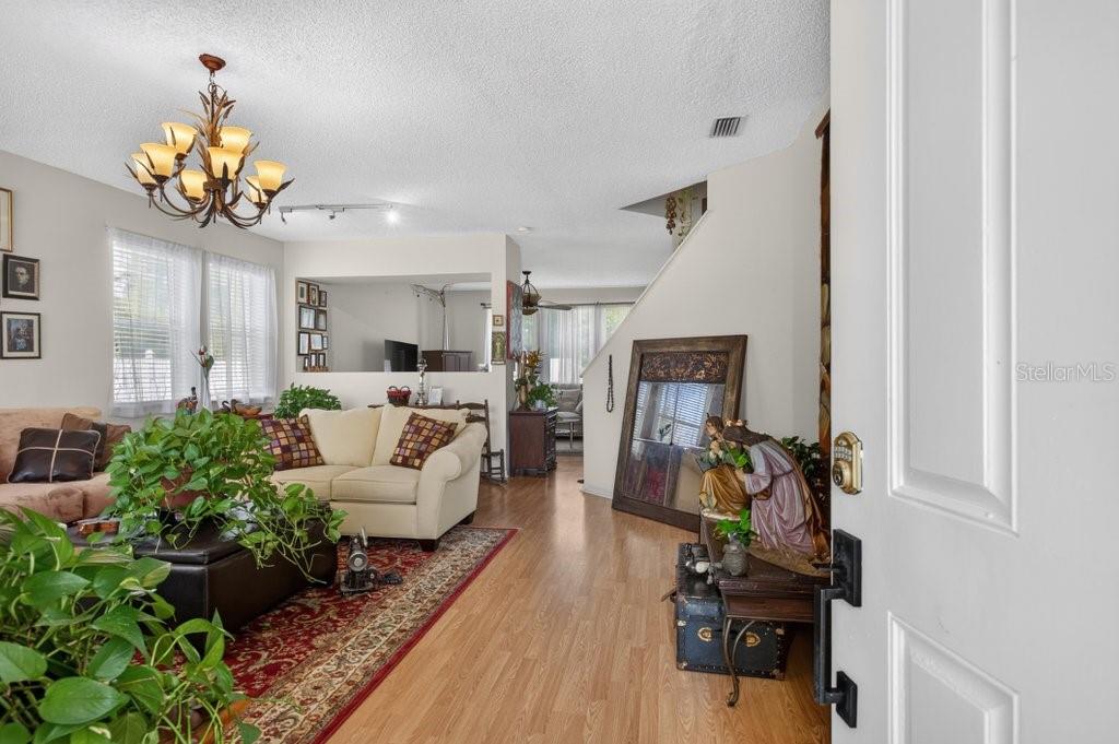 A living room features wood-look flooring, a chandelier, and a view into an adjacent area — 15 RYKER LANE, PALM COAST, FL