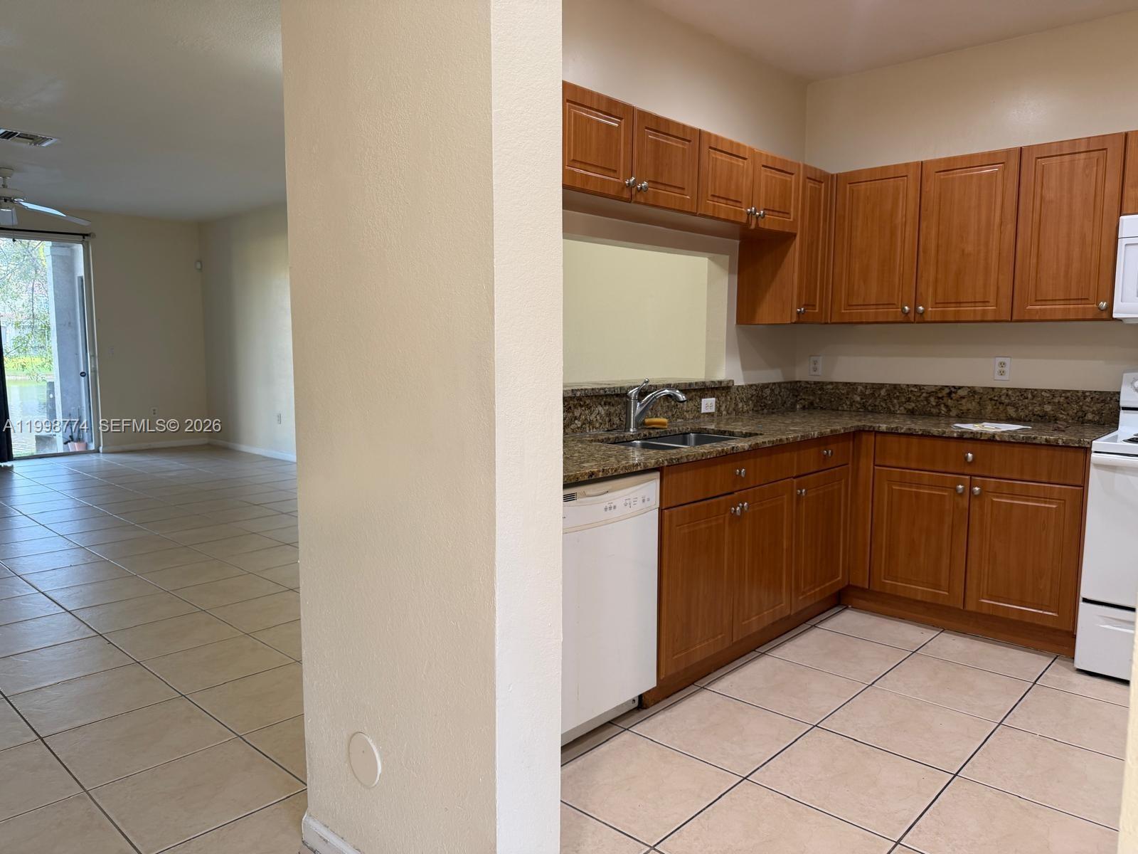 A kitchen with wood cabinets, granite countertops, and tile flooring opens to a living area — 8246 SW 27th St # 103, Miramar FL 33025, MIRAMAR, FL