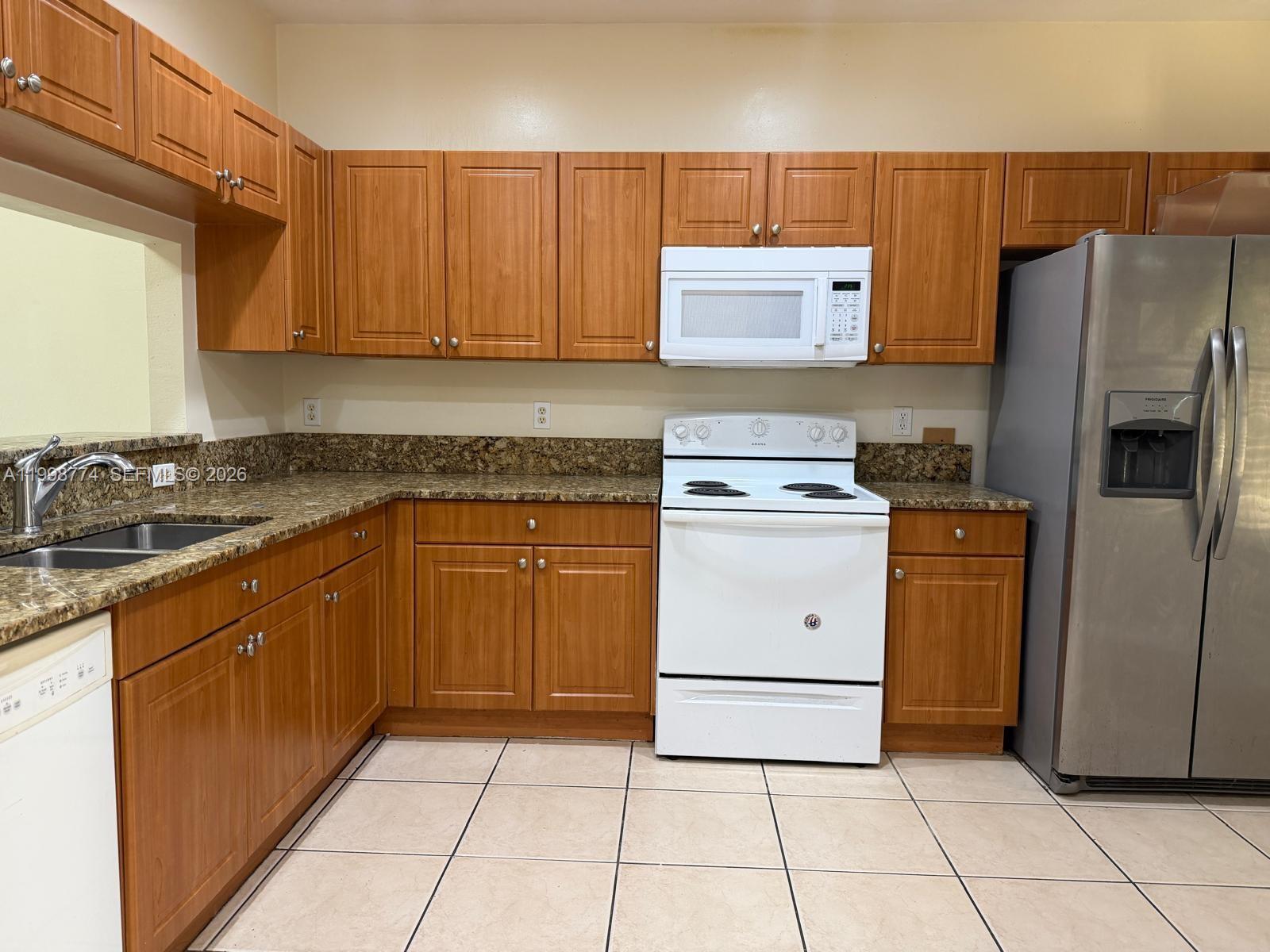 A kitchen features wood cabinets, granite countertops, white appliances, and a stainless steel refrigerator — 8246 SW 27th St # 103, Miramar FL 33025, MIRAMAR, FL