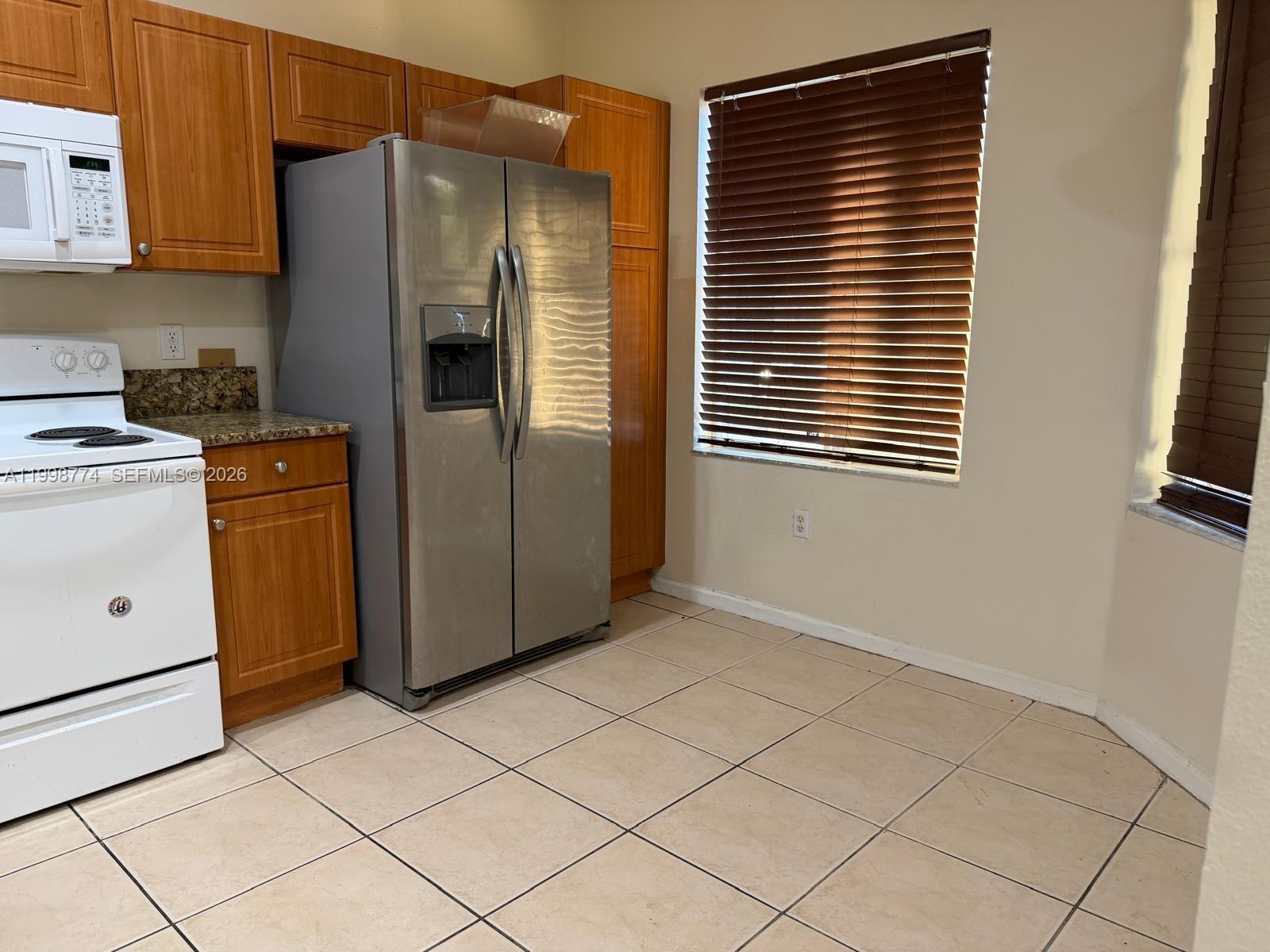 A kitchen features wood cabinets, stainless steel appliances, a white stove, and tiled flooring — 8246 SW 27th St # 103, Miramar FL 33025, MIRAMAR, FL