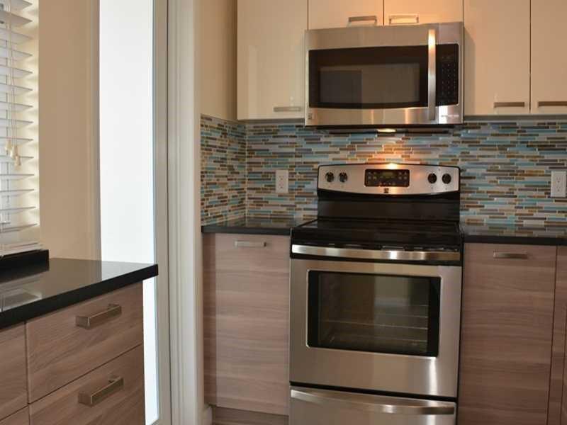 A kitchen features stainless steel appliances, wood-grain cabinets, and a multi-colored glass tile backsplash — 201 N Ocean Boulevard # 405, Pompano Beach FL 33062, POMPANO BEACH, FL