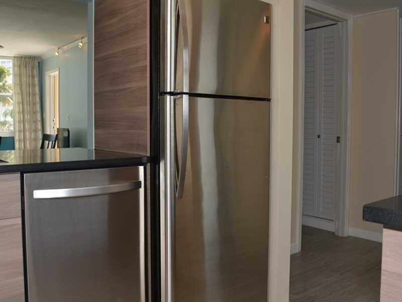 A stainless steel refrigerator and dishwasher are positioned in a kitchen with wood-toned cabinetry — 201 N Ocean Boulevard # 405, Pompano Beach FL 33062, POMPANO BEACH, FL