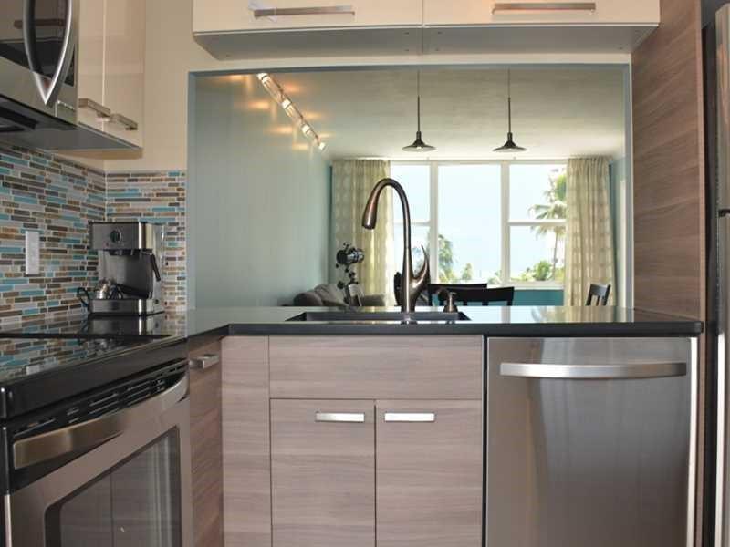 A modern kitchen features wood-grain cabinets, stainless steel appliances, and a tiled backsplash — 201 N Ocean Boulevard # 405, Pompano Beach FL 33062, POMPANO BEACH, FL