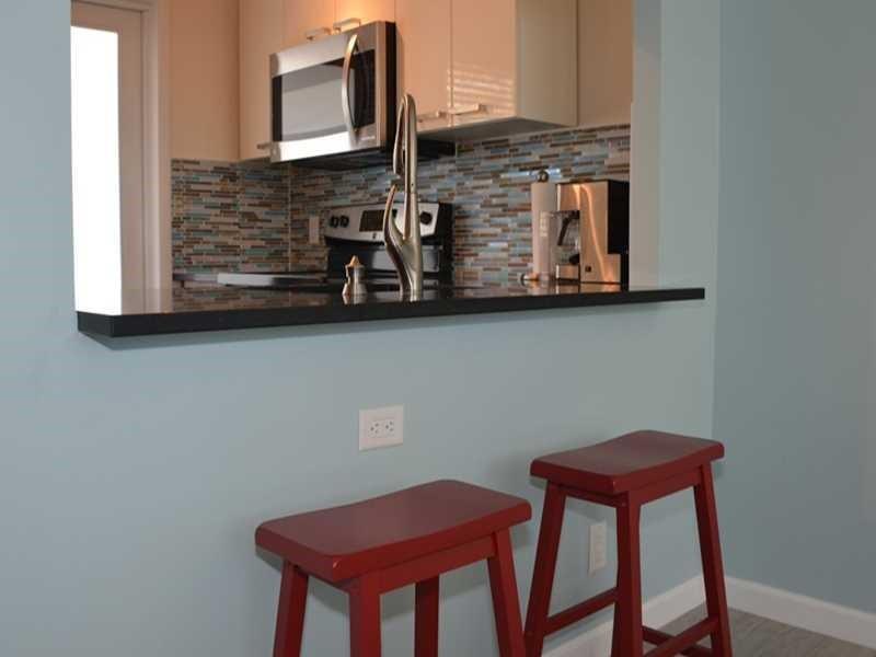 A kitchen pass-through features a black countertop, two red stools, and a glass tile backsplash — 201 N Ocean Boulevard # 405, Pompano Beach FL 33062, POMPANO BEACH, FL