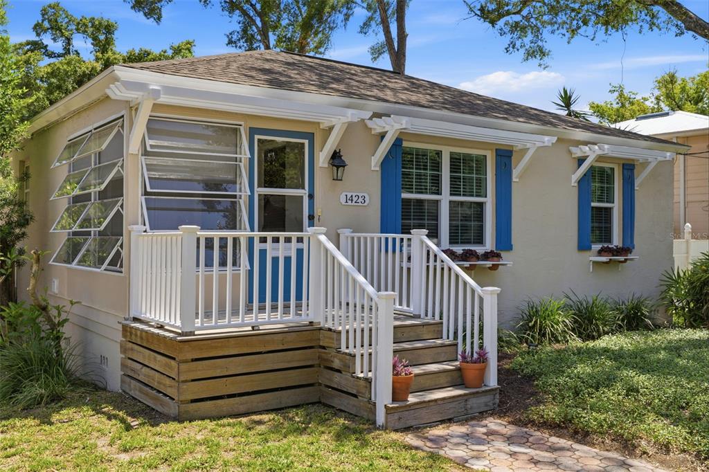 A small, beige, single-story house features a blue front door, white porch railing, and blue shutters — 1423 E HENRY AVENUE, TAMPA, FL