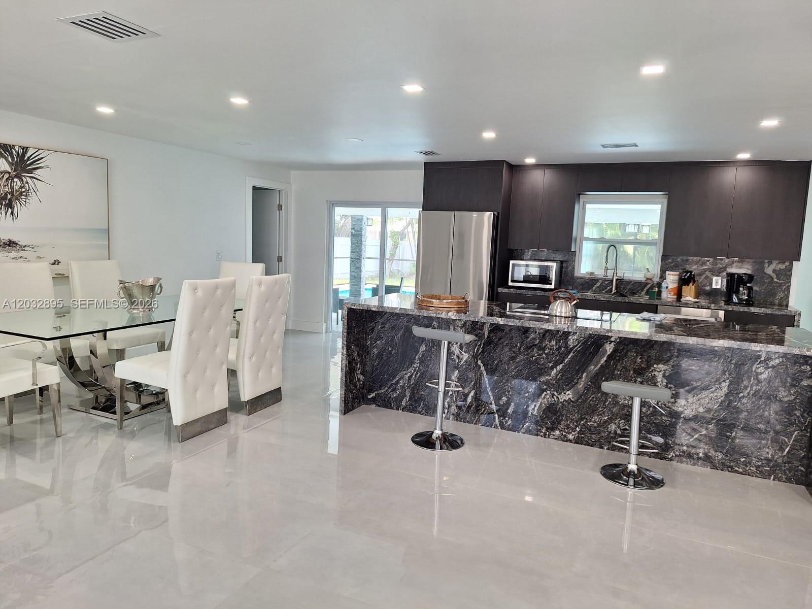 A modern kitchen features dark cabinetry, a dramatic black marble island, and an adjacent dining area — 4440 SW 14 pl, Cape Coral FL 339914, CAPE CORAL, FL