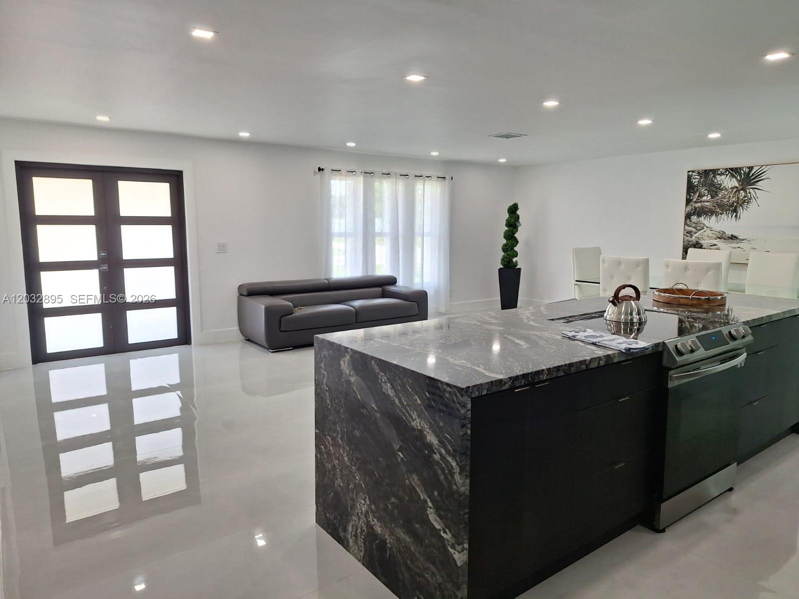 A modern kitchen features a dark stone island and white tile floors in an open space — 4440 SW 14 pl, Cape Coral FL 339914, CAPE CORAL, FL