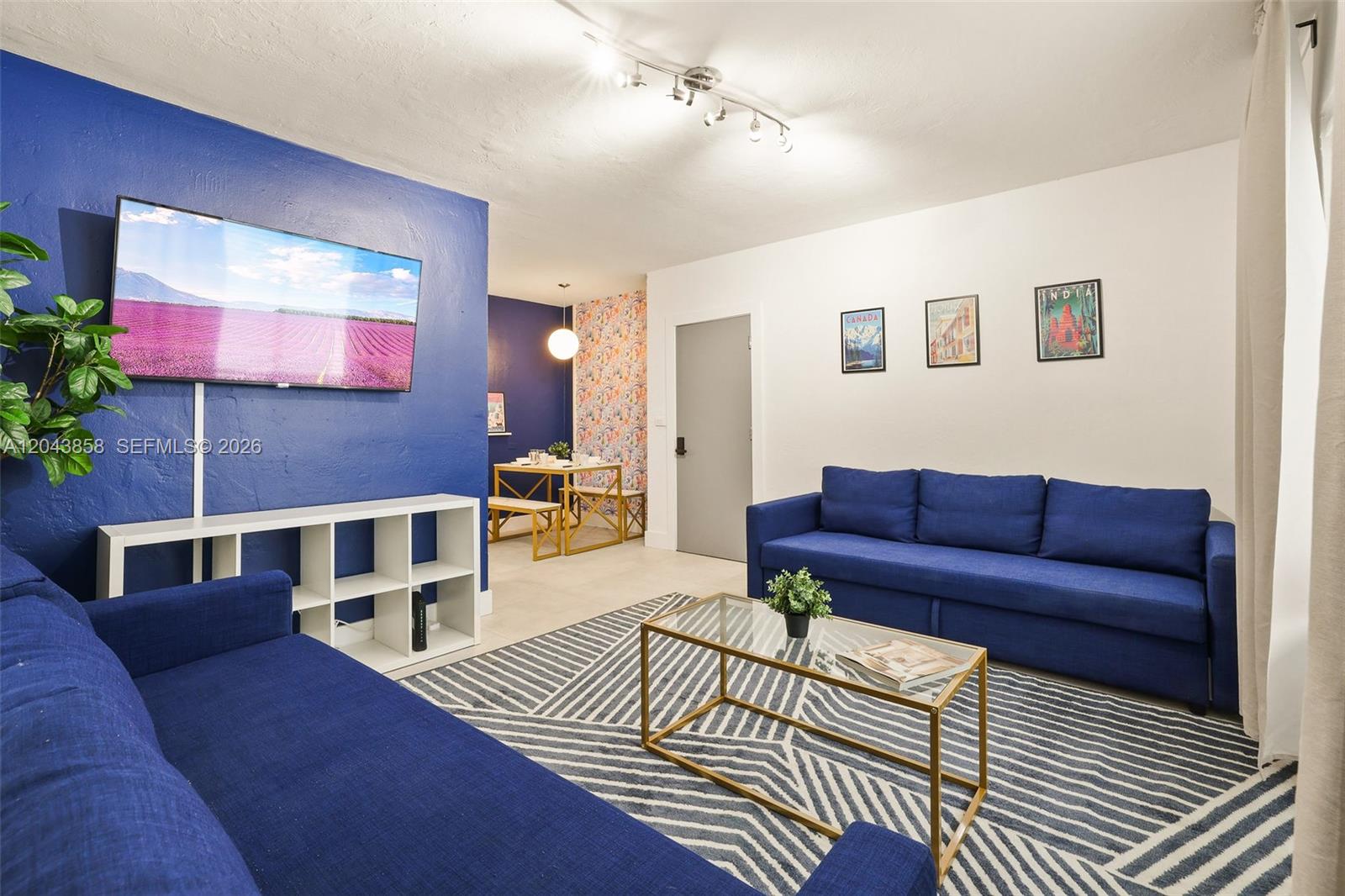 A living room features blue walls, two blue sofas, a patterned rug, and dining area — 7340 Harding Ave # 4, Miami Beach FL 33141, MIAMI BEACH, FL
