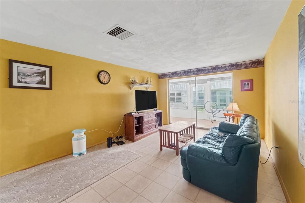 A living room with yellow walls, tile flooring, a dark leather sofa, and a television — 4211 REGAL PLACE UNIT 3, NEW PORT RICHEY, FL
