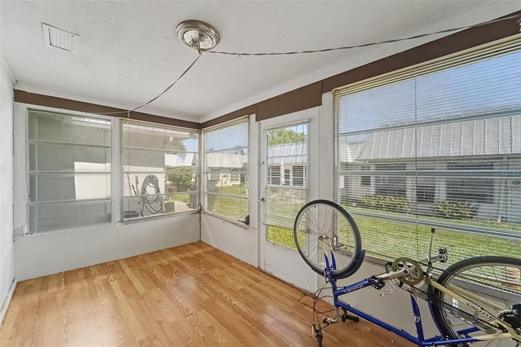 A sunroom with wood-look flooring, large windows with blinds, and a bicycle inside — 4211 REGAL PLACE UNIT 3, NEW PORT RICHEY, FL