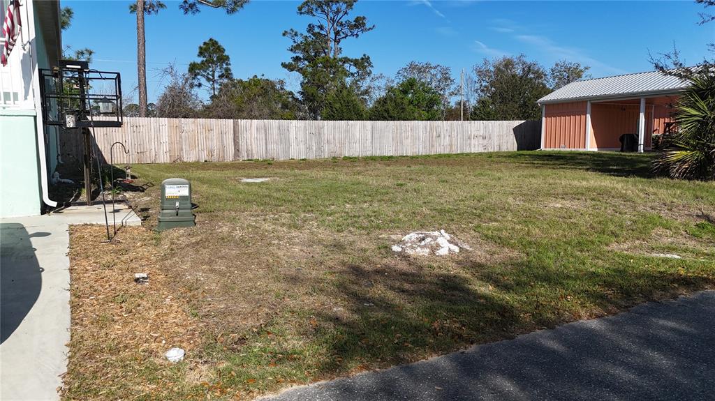 A grassy backyard features a wooden fence, a utility box, and a detached carport — Lot 44 SW 879TH STREET, STEINHATCHEE, FL
