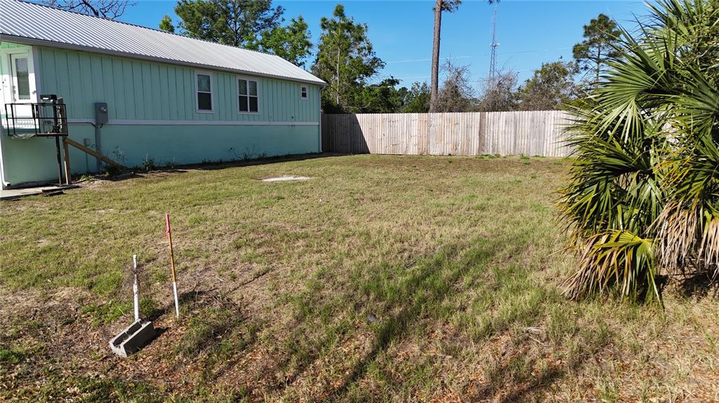 A grassy backyard features a light green house, a wooden fence, and a palm tree — Lot 44 SW 879TH STREET, STEINHATCHEE, FL
