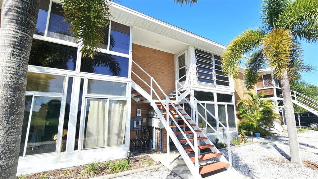 A two-story brick building features white-framed windows, an exterior staircase, and surrounding palm trees — 3586 CAPE HAZE DRIVE UNIT B4, ROTONDA WEST, FL