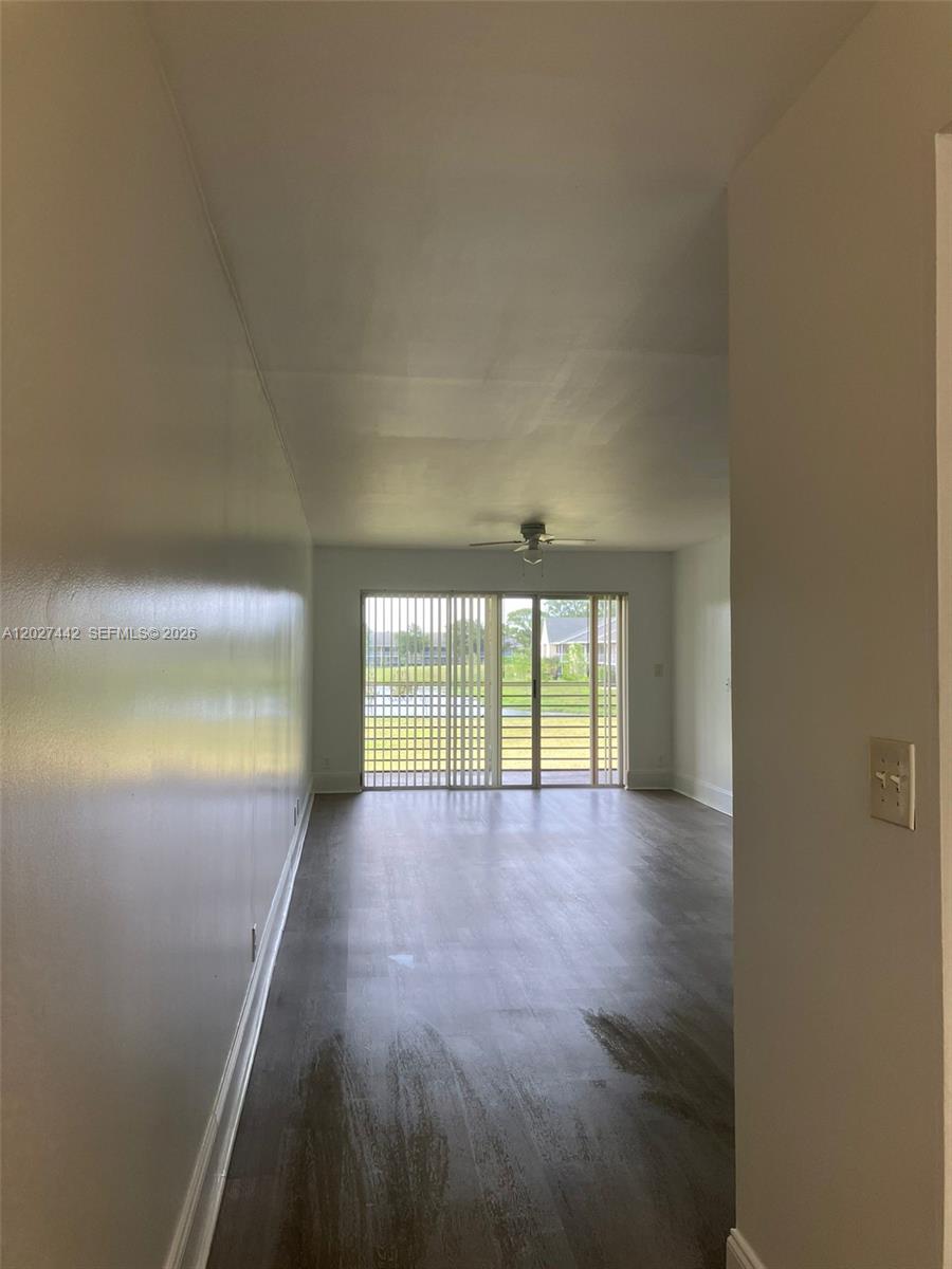 An empty room features dark wood-look flooring, a ceiling fan, and sliding glass patio doors — 2803 N Course Dr # 203, Pompano Beach FL 33069, POMPANO BEACH, FL