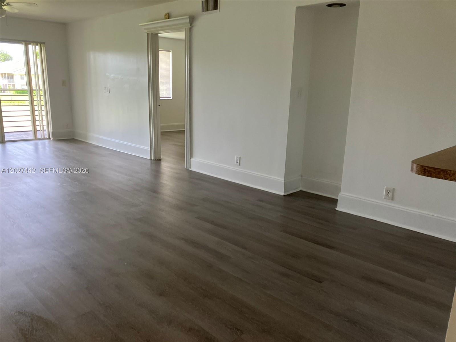 A living area features wood-look flooring, white walls, a sliding glass door, and an alcove — 2803 N Course Dr # 203, Pompano Beach FL 33069, POMPANO BEACH, FL