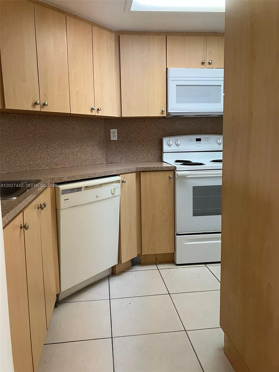 A kitchen features light wood cabinets, white appliances, and a tan countertop — 2803 N Course Dr # 203, Pompano Beach FL 33069, POMPANO BEACH, FL