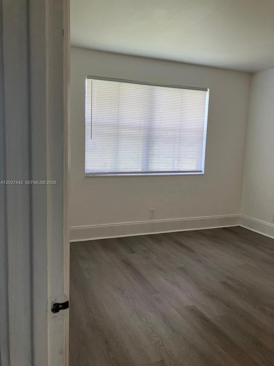 An empty bedroom features light-colored walls, wood-look flooring, and a window with white blinds — 2803 N Course Dr # 203, Pompano Beach FL 33069, POMPANO BEACH, FL