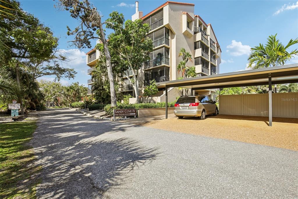 An exterior view of a multi-story apartment building with a covered parking area and trees — 4900 OCEAN BOULEVARD UNIT 201, SARASOTA, FL